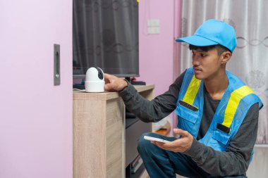 Asyalı erkek teknisyen, müşterinin evindeki akıllı telefonu kullanarak CCTV veya kablosuz güvenlik kameralarını kurar ve kurar.