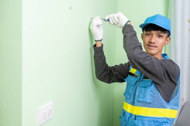 Asyalı erkek işçi alçı taşı duvarındaki vidaları sıkmak için tornavida kullanıyor.