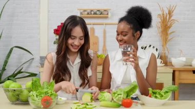 Siyah ve beyaz genç arkadaşlar mutfakta sebze salatası yapmak için birlikte çalışıyorlar. Sağlıklı yemek..