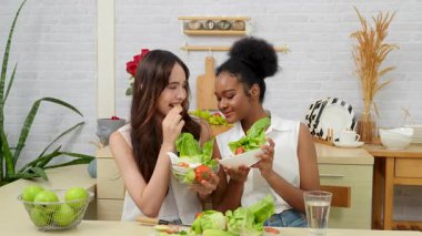 Siyah ve beyaz genç arkadaşlar mutfakta sebze salatası yapmak için birlikte çalışıyorlar. Sağlıklı yemek..