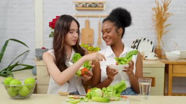 Siyah ve beyaz genç arkadaşlar mutfakta sebze salatası yapmak için birlikte çalışıyorlar. Sağlıklı yemek..