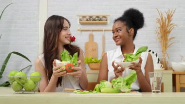 Siyah ve beyaz genç arkadaşlar mutfakta sebze salatası yapmak için birlikte çalışıyorlar. Sağlıklı yemek..