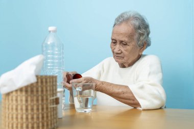 Yaşlı bir Asyalı kadın ilaç hazırlamak için plastik şişeden ilaç döküyor..