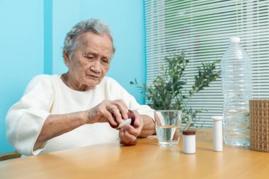 Yaşlı bir Asyalı kadın ilaç hazırlamak için plastik şişeden ilaç döküyor..