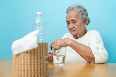 Yaşlı bir Asyalı kadın ilaç hazırlamak için plastik şişeden ilaç döküyor..