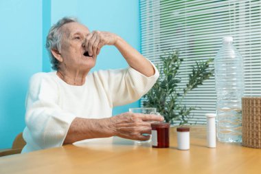 Yaşlı bir Asyalı kadın ilaç hazırlamak için plastik şişeden ilaç döküyor..