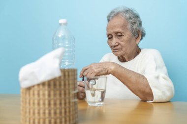 Yaşlı bir Asyalı kadın ilaç hazırlamak için plastik şişeden ilaç döküyor..
