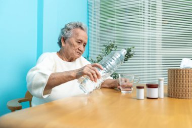 Yaşlı bir Asyalı kadın ilaç almaya hazırlanmak için plastik şişeden bardağa su dolduruyor..
