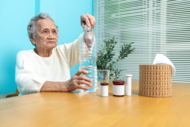 Yaşlı bir Asyalı kadın ilaç almaya hazırlanmak için plastik şişeden bardağa su dolduruyor..