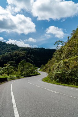 Curved asphalt road in mountain range with blue sky. Cloudy sky with the highland road on summer day. Mountain highway with forest landscape. Winding road. Outdoors travel, trip, countryside concept