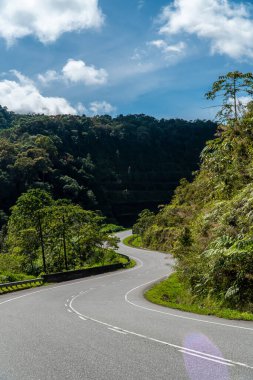 Curved asphalt road in mountain range with blue sky. Cloudy sky with the highland road on summer day. Mountain highway with forest landscape. Winding road. Outdoors travel, trip, countryside concept