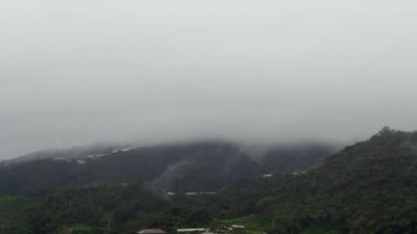 Bir köyün ve dağın üzerinde süzülen bulut. Sisli sis, ağaç ormanının üzerinde esiyor. Ormanda yağmur, duman, yağmur ormanlarında sisli hava. Zaman Uygulaması