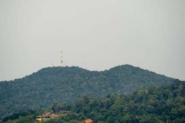 Yeşil dağın tepesindeki iletişim kulesi. Dağ tepesindeki radyo kulesi. Yağmur ormanları dağının manzarası. Tepedeki köy