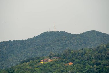 Yeşil dağın tepesindeki iletişim kulesi. Dağ tepesindeki radyo kulesi. Yağmur ormanları dağının manzarası. Tepedeki köy