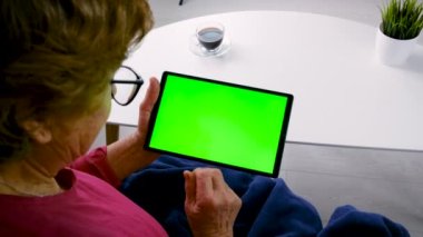 Yaşlı kadın tablet yeşili arka plana bak. Seçici odaklanma. yeşil