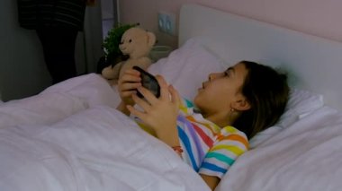 Anne yatakta bir tabletle bir çocuğu azarlar. Seçici odaklanma. Çocuk.