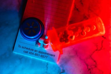 Birisine ilaç içeren ilaç şişesi aç. Reçeteli kağıdın üstünde neon lambaları var.
