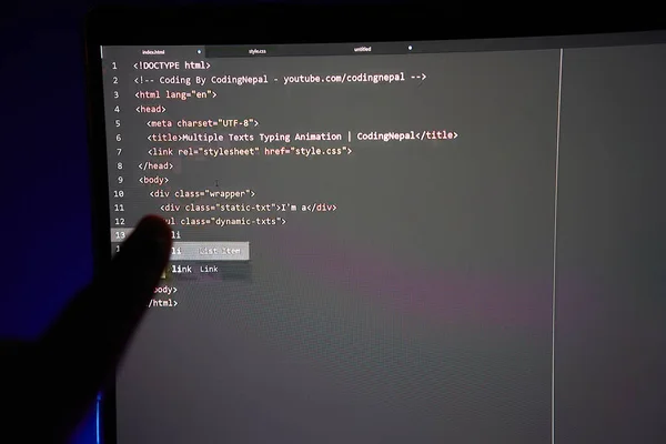 Writing computer code displayed on monitor pointing finger at a line of code