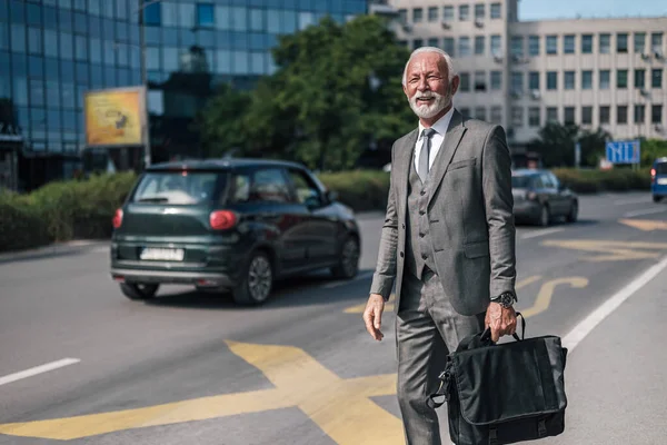 Smiling elderly businessman carrying laptop bag while hailing for taxi cab. Male professional is waiting for ride on roadside while commuting in city. He is in suit during sunny day.