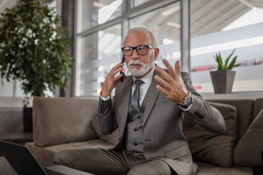 Akıllı telefondan tartışırken kafası karışmış profesyonel erkek jestleri. Kıdemli iş adamı kanepede otururken masada dizüstü bilgisayar kullanıyor. Ofiste çalışırken takım elbise giyiyor..