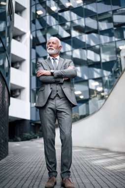 Kolları bağlı kendinden emin bir profesyonel başka tarafa bakıyor. Yaşlı işadamlarının tamamı ofis binasının önünde duruyor..