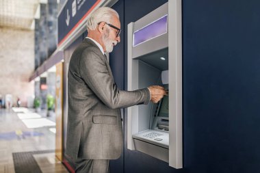 ATM kullanan kıdemli girişimcinin profil görüntüsü. Yaşlı işadamı şehirde işe gidip gelirken elektronik bankacılık yoluyla para çekiyor..