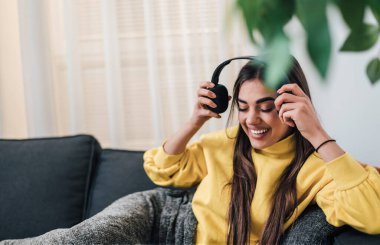 Oyuncu, uzun saçlı bir kadın, kulaklıklarını çıkarıyor, rahatlarken gülümsüyor..