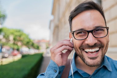 Enerjik bir genç adam, dışarıda yürürken müzik dinlemeye hazırlanıyor..