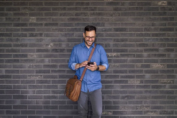Szczęśliwy Dorosły Mężczyzna Sprawdzający Kontakty Telefoniczne Podczas Odpoczynku Przy Ścianie — Zdjęcie stockowe