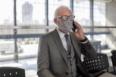 Kıdemli işadamı maske takıyor ve akıllı telefondan konuşuyor. Yaşlı erkek girişimci Corona virüsü salgını sırasında metro istasyonunda bekliyor. Koruyucu tedbirler alıyor..