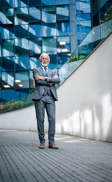 stock image Full length of businessman standing with arms crossed on walkway against business office building.