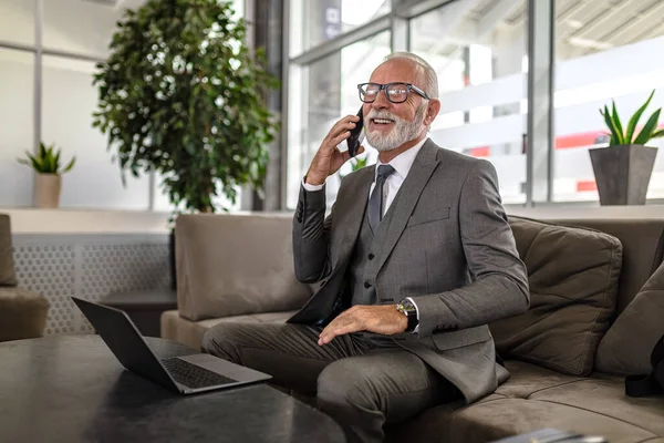 Успешный Бизнесмен Разговаривает Смартфоне Используя Ноутбук Офисном Зале — стоковое фото