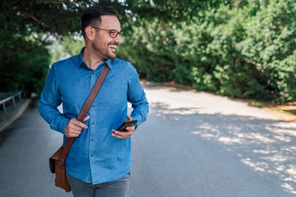 Ενθουσιασμένος Ενήλικας Μπλε Πουκάμισο Κρατώντας Τηλέφωνό Του Περπατώντας Στο Πάρκο — Φωτογραφία Αρχείου
