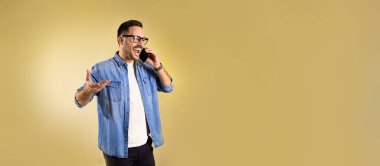 Yakışıklı adam cep telefonuyla gülüyor ve konuşuyor. Neşeli erkek eğlenceli sohbet ediyor. Sıradan bir kot elbise giyiyor..