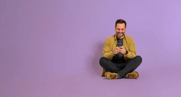 Šťastný Muž Zprávy Pomocí Chytrého Telefonu Fialovém Pozadí Sedí Zkříženýma — Stock fotografie
