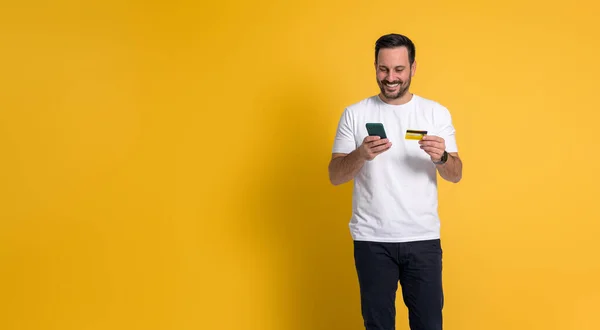 stock image Smiling man doing online shopping with mobile phone and credit card. Happy guy ordering from e commerce or social media. He is paying for his purchase