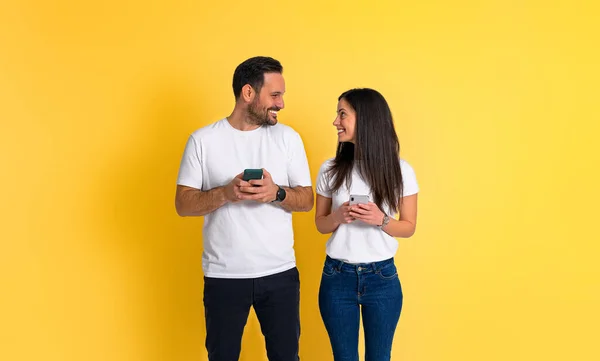 可爱的年轻夫妇 穿着白色的T恤衫 手持手机 面面相觑 站在黄色的背景下 — 图库照片