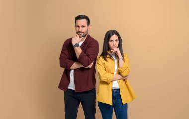 Cazibeli giyinmiş, çenelere dokunan ve izole edilmiş bej arka planda duran çekici bir kadın ve erkek. Kameraya bakarken poz veren çift portresi