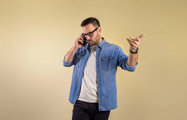 stock image Frustrated male entrepreneur discussing serious problem over mobile phone. Stressed young man making call and gesturing against isolated beige background