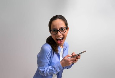 Heyecanlı bayan girişimcinin portresi neşeli bir şekilde bağırıyor ve internette akıllı telefondan mesajlaşıyor. Gözlük takan mest olmuş bir iş kadını cep telefonunu izole edilmiş arka planda kullanıyor.