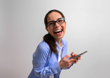 Başarılı iş kadını akıllı telefondan iyi haberleri okuduktan sonra sevinçle gülüyor. Arka planda cep telefonuyla mesajlaşan neşeli genç bayan profesyonel.