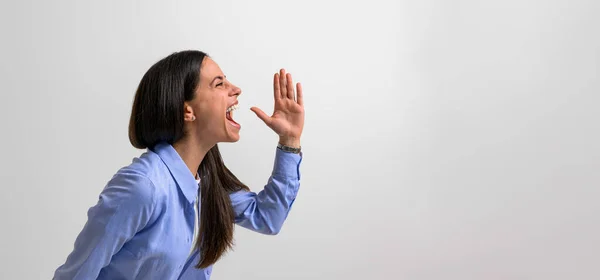 stock image Side view of successful female professional screaming and gesturing in joy while standing isolated on background. Young businesswoman dressed in casuals showing hand sign and shouting