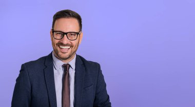 Gözlüklü, şık takım elbiseli ve kameraya bakan yakışıklı, neşeli, profesyonel şef portresi. Neşeli gülümseyen ve mavi arka planda poz veren mutlu iş adamı
