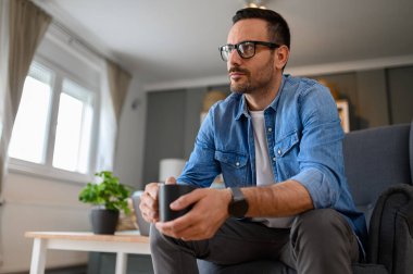 Ciddi bir iş adamının elinde kahve fincanı tutarak koltukta otururken tefekküre dalması. Erkek serbest çalışan, içki içen ve ofisten çalışırken iş fikirleri düşünen biri.