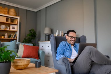 Gülümseyen yakışıklı serbest yazar evdeki koltukta dinlenirken kablosuz bilgisayardan e-postaları kontrol ediyor. Genç erkek girişimci ev ofisinde rahatça otururken dizüstü bilgisayarın üzerinde sörf yapıyor.