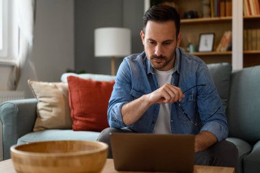 Gözlük tutan odaklanmış erkek bilgisayar programcısı ve koltukta otururken laptop üzerinde ciddi şekilde çalışıyor. Dahili ofisten uzaktan kumandalı kablosuz bilgisayarda kodlama yapan genç düşünceli bir serbest yazar.