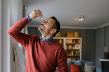 Genç adam evde dikilirken kuru göz veya alerjiyi tedavi etmek için göz kremi kullanıyor.