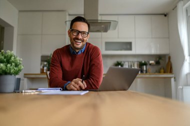 Gözlüklü gülümseyen yakışıklı iş adamının portresi ofis masasında dizüstü bilgisayarla çalışıyor.