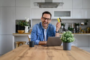 Kredi kartı tutan ve internetten alışveriş yapan neşeli iş adamının portresi.