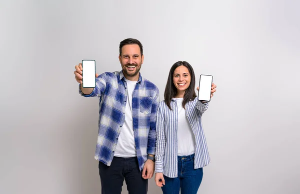 stock image Young couple smiling and showing blank screens of smart phones for advertisements. Cheerful man and woman promoting cellphones with empty free space against background